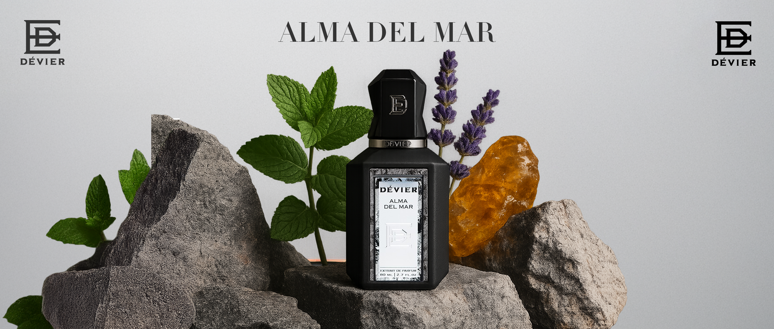 A matte black bottle of Dévier “Alma del Mar” rests among rugged stones, fresh mint, amber resin, and lavender—capturing the essence of sea breeze, nature, and refined strength.