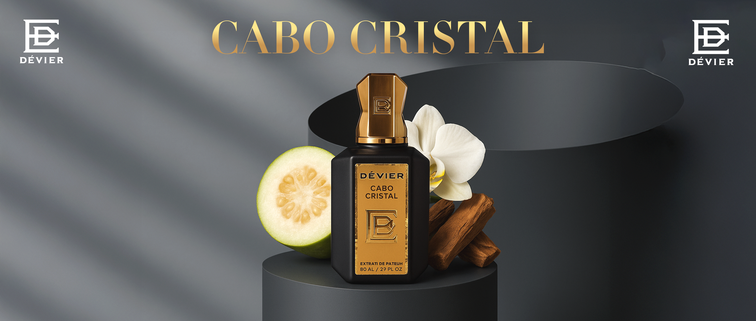 A luxurious black and gold bottle of Dévier “Cabo Cristal” perfume sits elegantly beside guava, vanilla flower, and cinnamon on a sleek dark backdrop, conveying richness and sophistication.